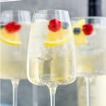 Pinterest graphic for White Wine Spritzer recipe. Text says, "the best wine spritzer simplejoy.com." Image is photo of White Wine Spritzers garnished with lemon wedges and berries. Extra lemon wedges and berries on counter beside glasses.