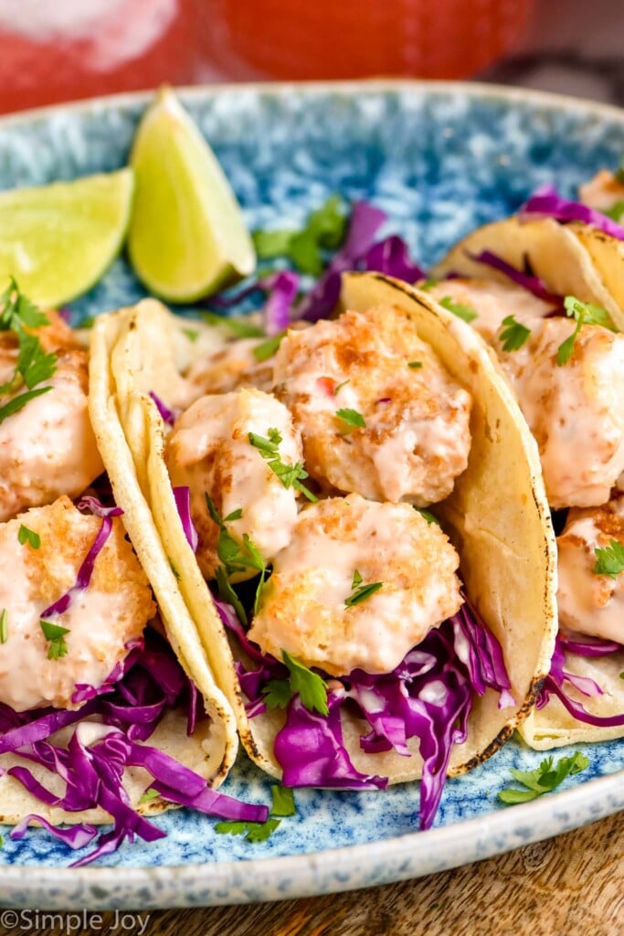 Close up photo of Bang Bang Shrimp Tacos with lime wedges for garnish.