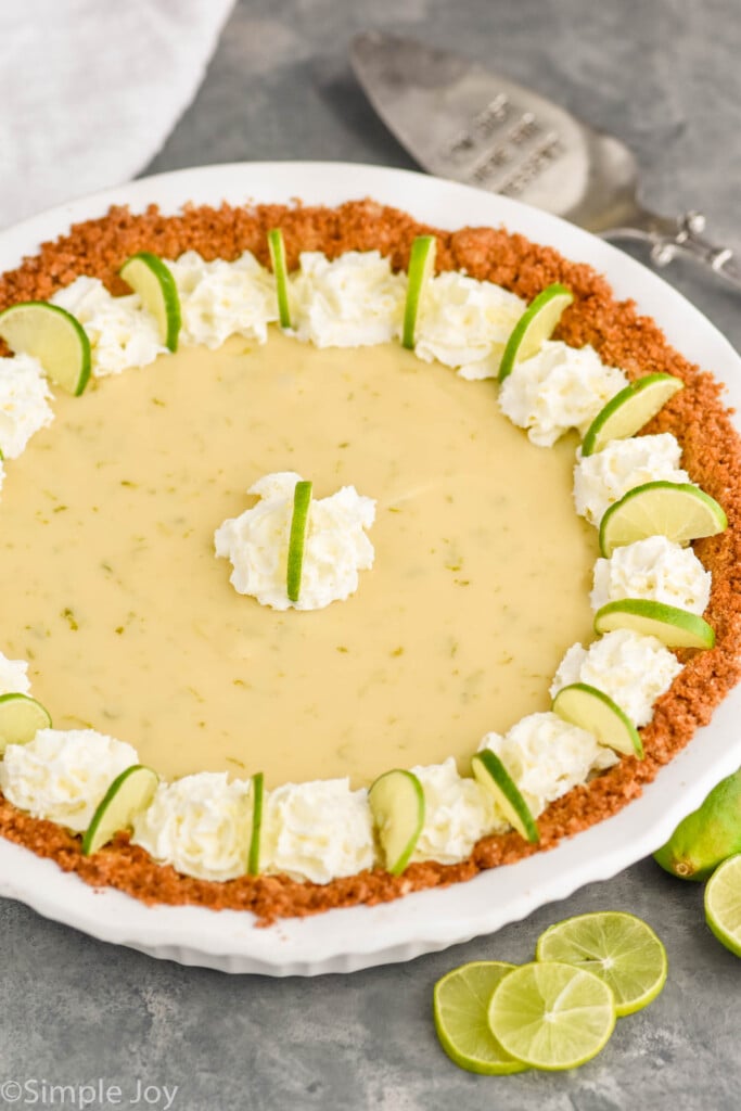 Overhead photo of Key Lime Pie. Lime slices for garnish and a serving spatula on counter beside Key Lime Pie.