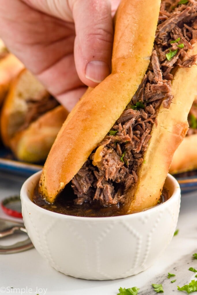 Photo of person's hand dipping French Dip Sandwich into a bowl of drippings.