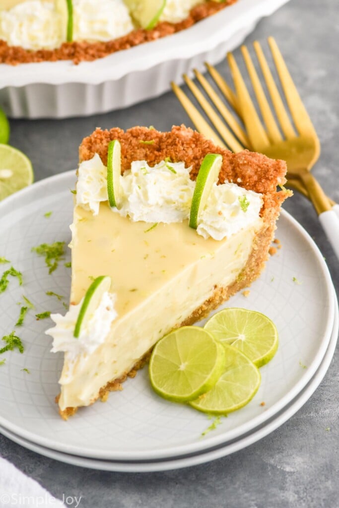 Overhead photo of a slice of Key Lime Pie served on a plate, garnished with lime slices. Forks on counter beside plate.