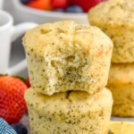 Close up photo of two Lemon Poppy Seed Muffins stacked on top of each other, with a bite taken out of the top muffin. Bowl of berries in the background. - 9