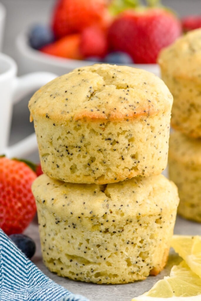 Photo of a stack of two Lemon Poppy Seed Muffins. Bowl of berries in the background.