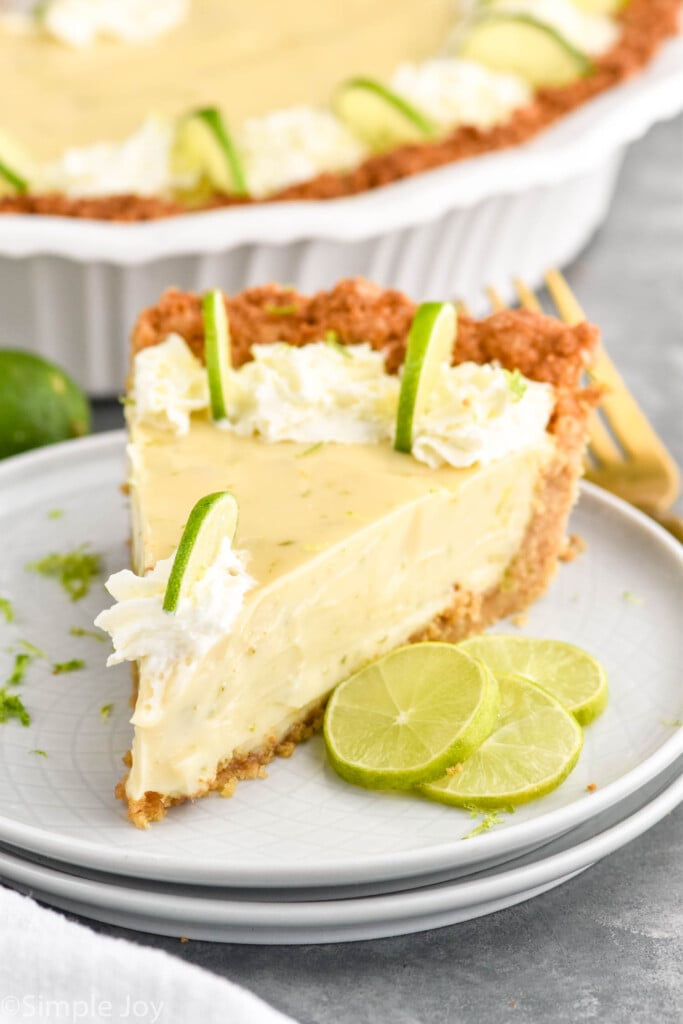 Photo of a slice of Key Lime Pie on a plate garnished with slices of lime. Key Lime Pie is in the background.