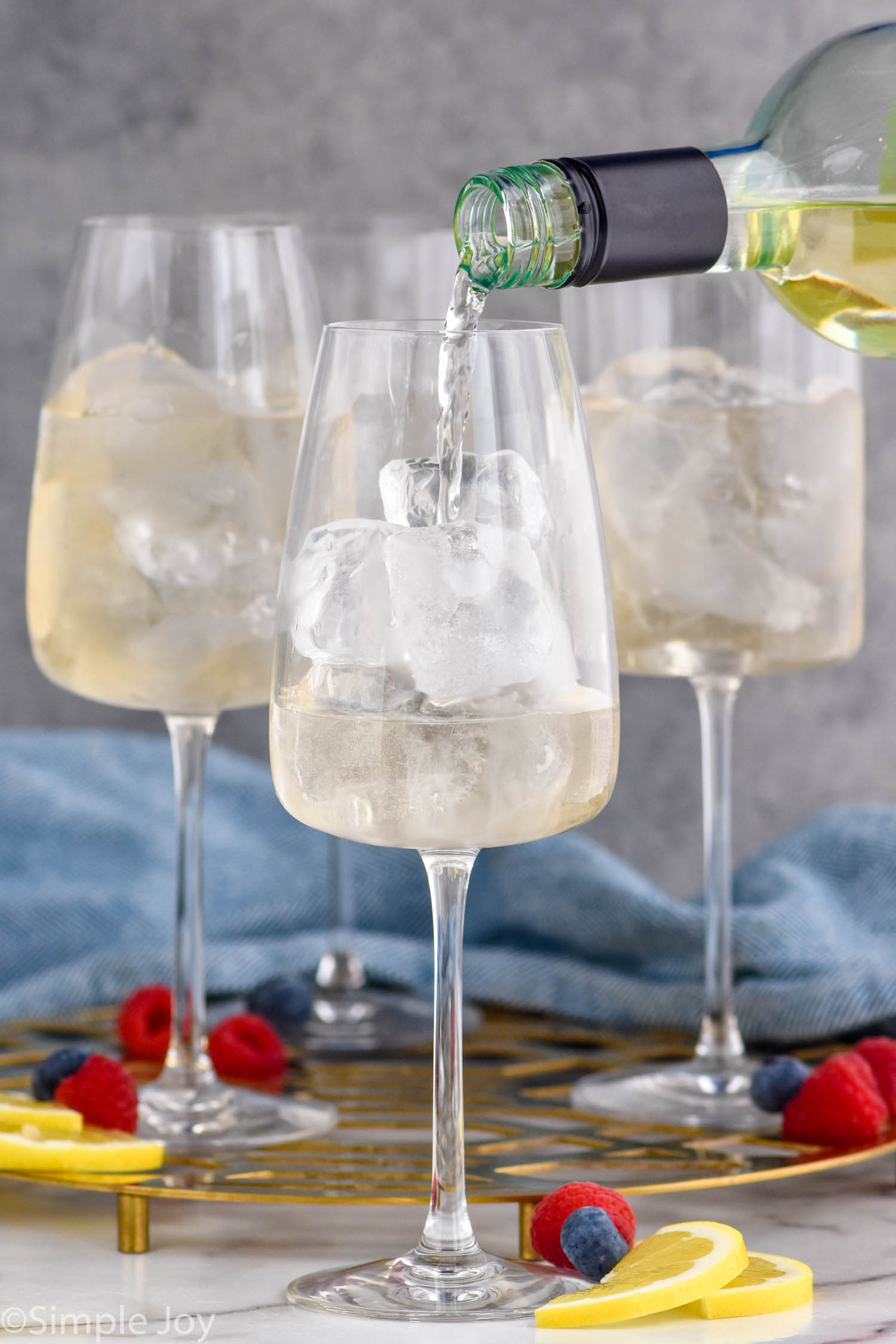Photo of glasses of ice and wine being poured into glasses for White Wine Spritzer recipe.