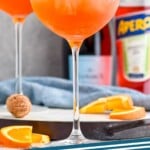 Pinterest graphic for Aperol Spritz recipe. Image is close up photo of Aperol Spritz cocktails garnished with orange slices. Bottles of sparkling wine and aperol in the background. Text says, "Aperol Spritz simplejoy.com"