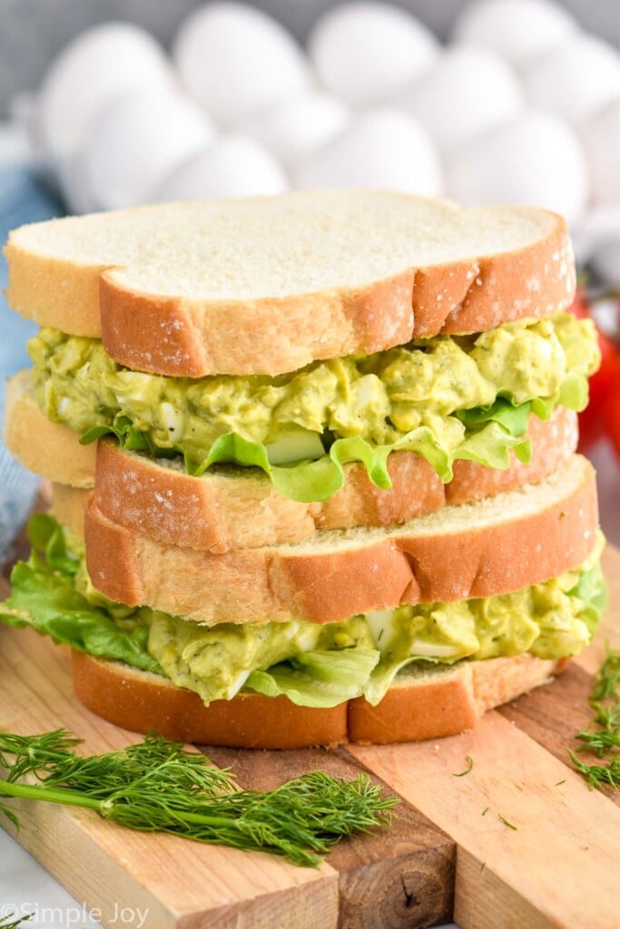 Photo of a stack of two Avocado Egg Salad sandwiches. Eggs in background.