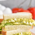 Pinterest graphic for Avocado Egg Salad recipe. Text says, "The best Avocado Egg Salad simplejoy.com." Image is close up photo of a stack of two Avocado Egg Salad sandwiches cut in half.