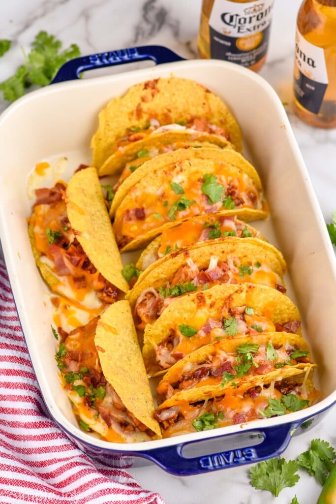 Overhead photo of a baking dish of BBQ Chicken Baked Tacos. Two bottles of beer sit beside baking dish of BBQ Chicken Baked Tacos.