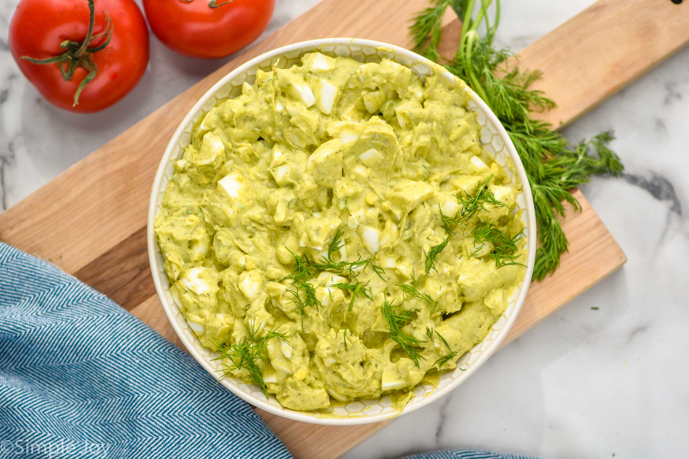 Overhead photo of a bowl of Avocado Egg Salad with tomatoes beside bowl.