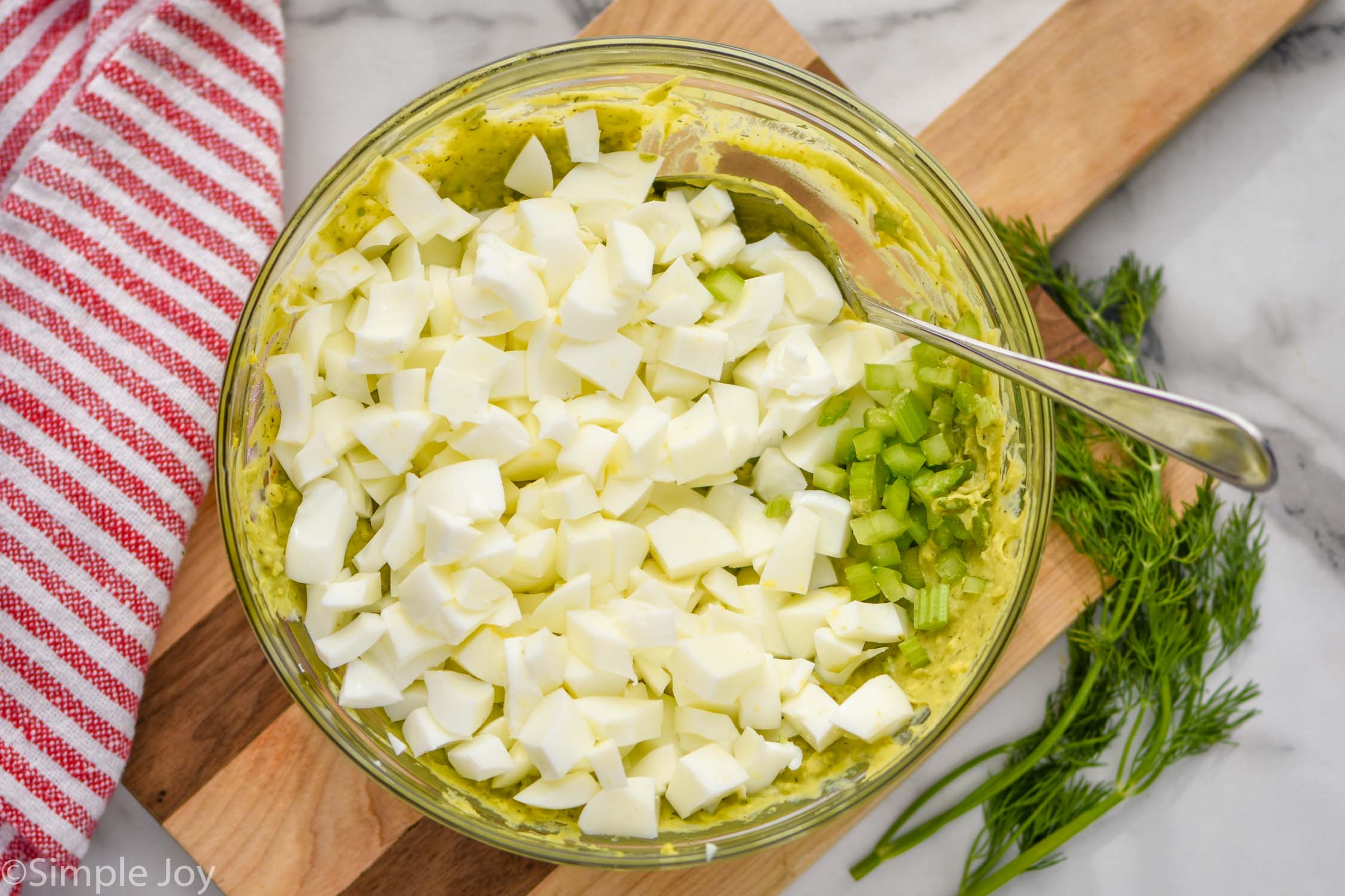 Overhead photo of a bowl of ingredients for Avocado Egg Salad recipe with spoon for mixing.