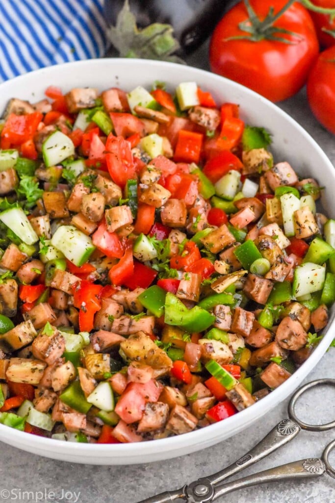 Overhead photo of Eggplant Salad in a bowl. Salad tongs and tomatoes beside bowl of Eggplant Salad.