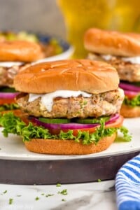Close up photo of Greek Turkey Burgers served on buns with yogurt sauce, lettuce, tomato, onion, and pickles.