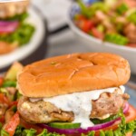 Pinterest graphic for Greek Turkey Burgers. Text says, "Amazing Greek Burgers simplejoy.com." Close up photo of Greek Turkey Burgers served on buns with yogurt sauce, lettuce, tomato, onion, and pickles.