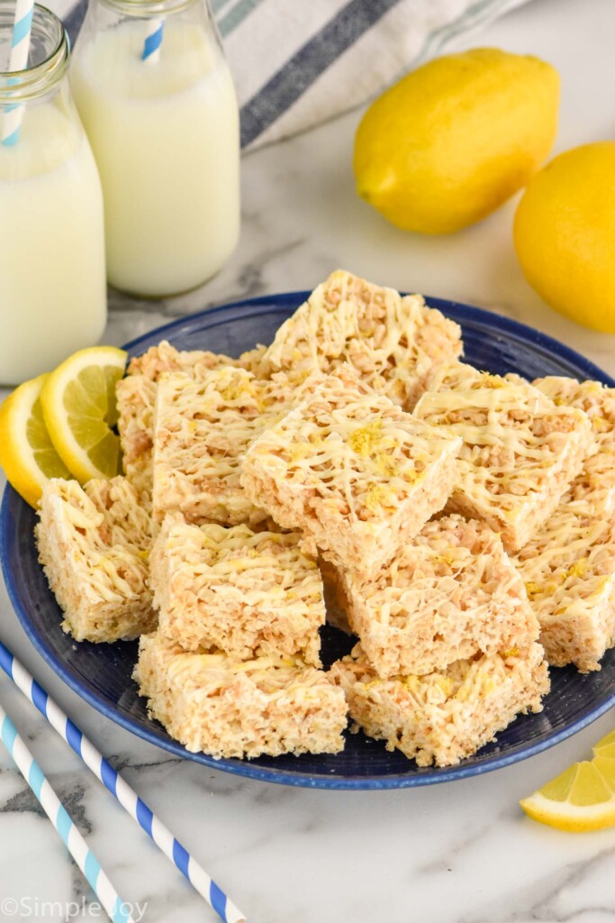 Overhead photo of a plate of Lemon Rice Krispie Treats. Glasses of milk and lemons beside plate.