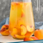 Pinterest graphic for Peach Sangria Recipe. Image is photo of a pitcher of Peach Sangria with extra peaches on the side. Text says, "Peach Sangria simplejoy.com."