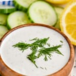 Pinterest graphic for Yogurt Sauce recipe. Text says, "super easy Yogurt Sauce simplejoy.com." Image is close up photo of a bowl of Yogurt Sauce garnished with dill. Dill, cucumber slices, and lemons sit beside bowl.