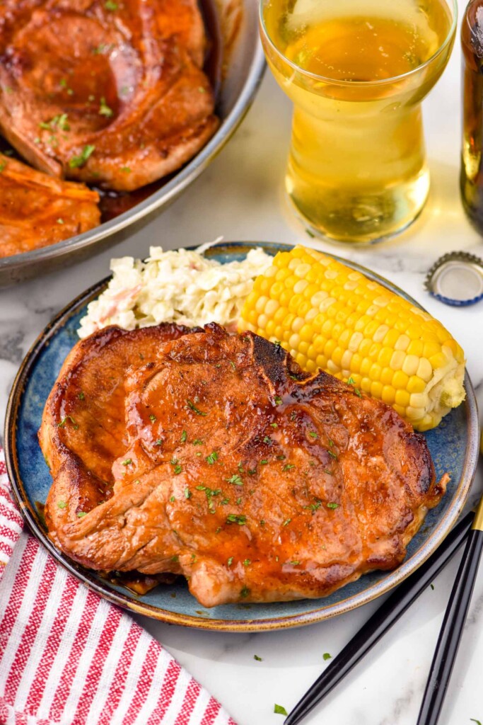 Overhead photo of BBQ Pork Chops served on a plate with corn on the cob and mashed potatoes. Glass of beer next to plate.