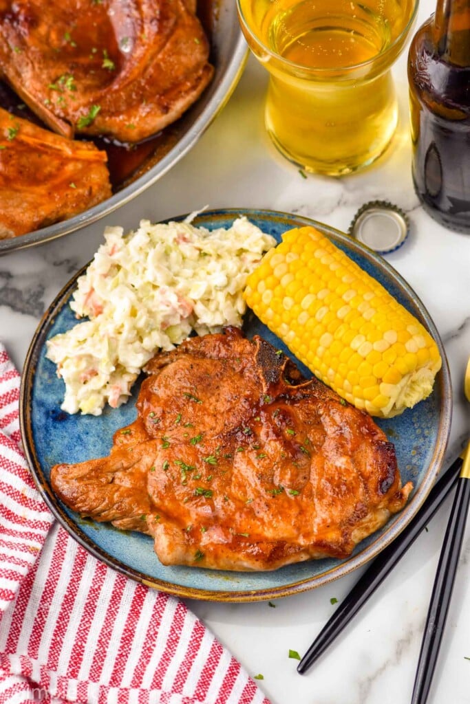 Overhead photo of BBQ Pork Chops served on a plate with corn on the cob and mashed potatoes. Glass of beer next to plate.