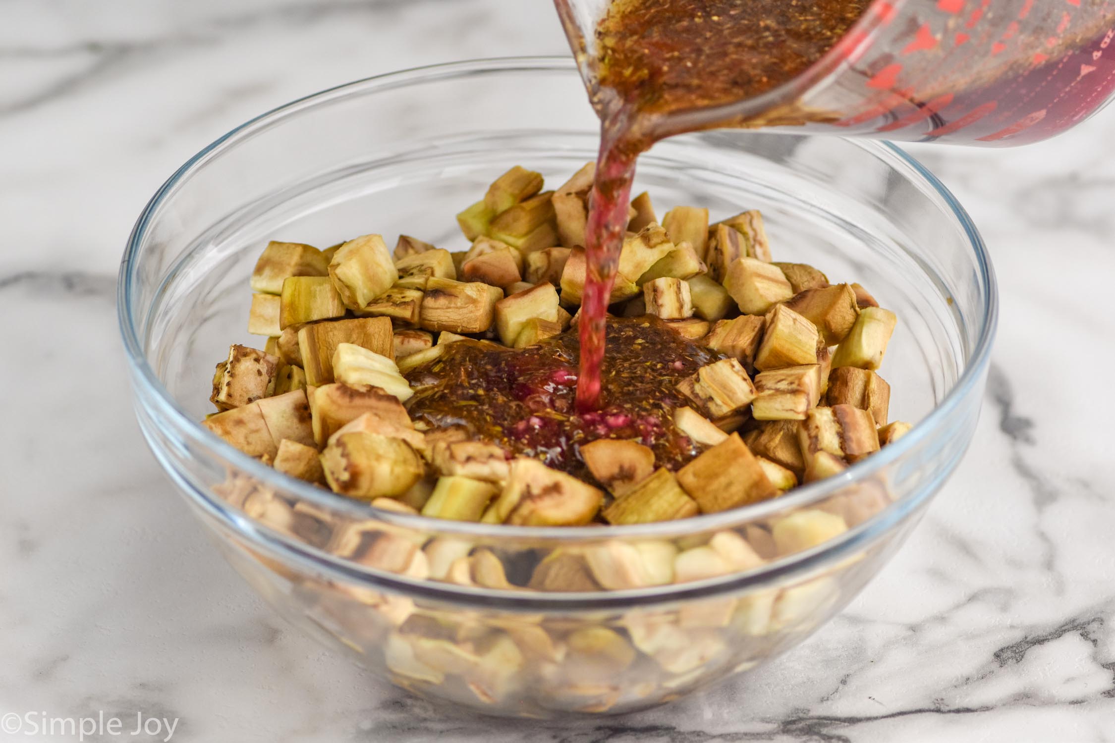 Photo of measuring cup of ingredients being poured into bowl of prepared eggplant for Eggplant Salad recipe.