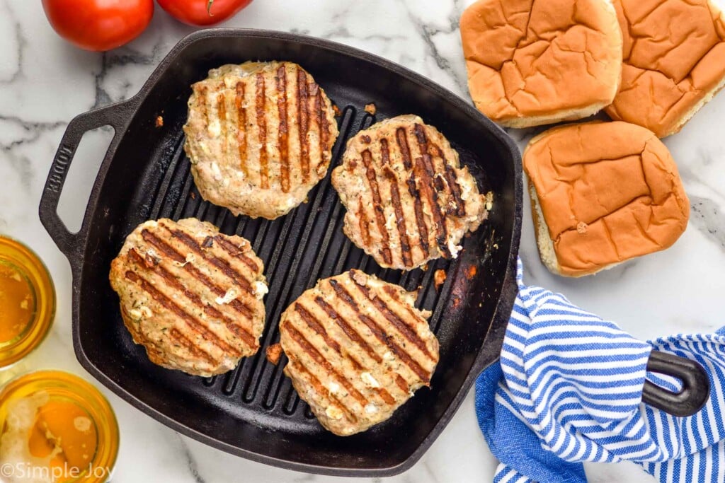 Overhead photo of Greek Turkey Burgers in a skillet. Buns and two glasses of beer beside skillet.