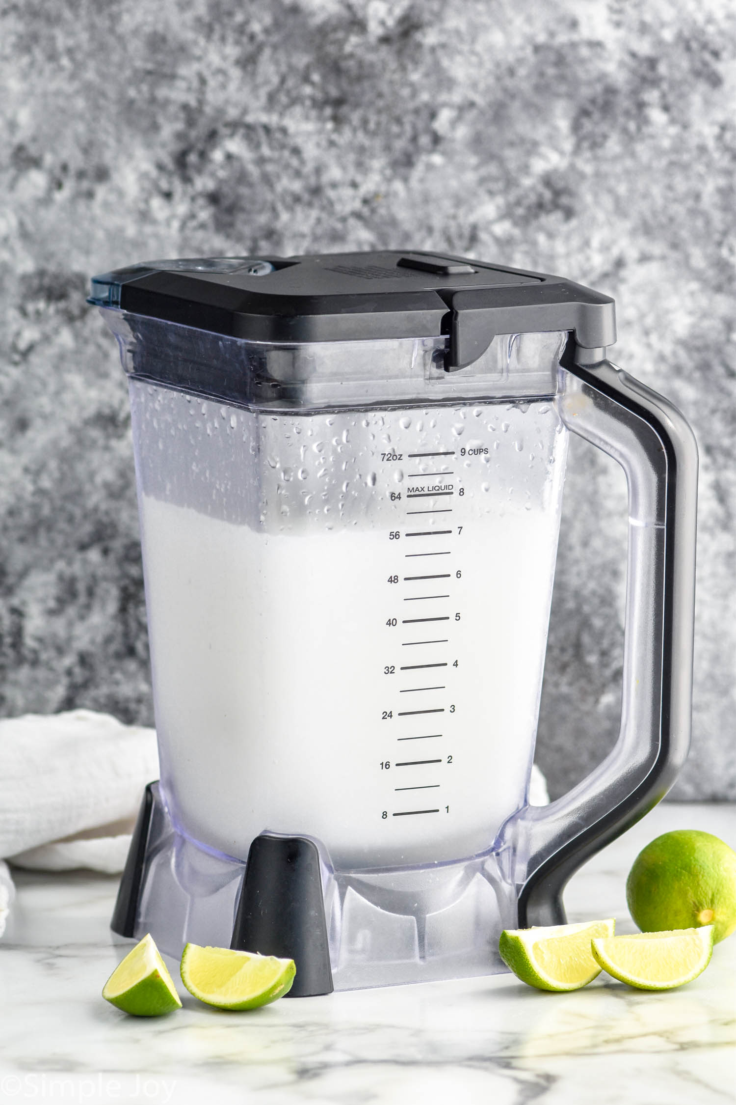 Photo of a blender of ingredients for Frozen Margaritas. Lime wedges beside blender for garnish.