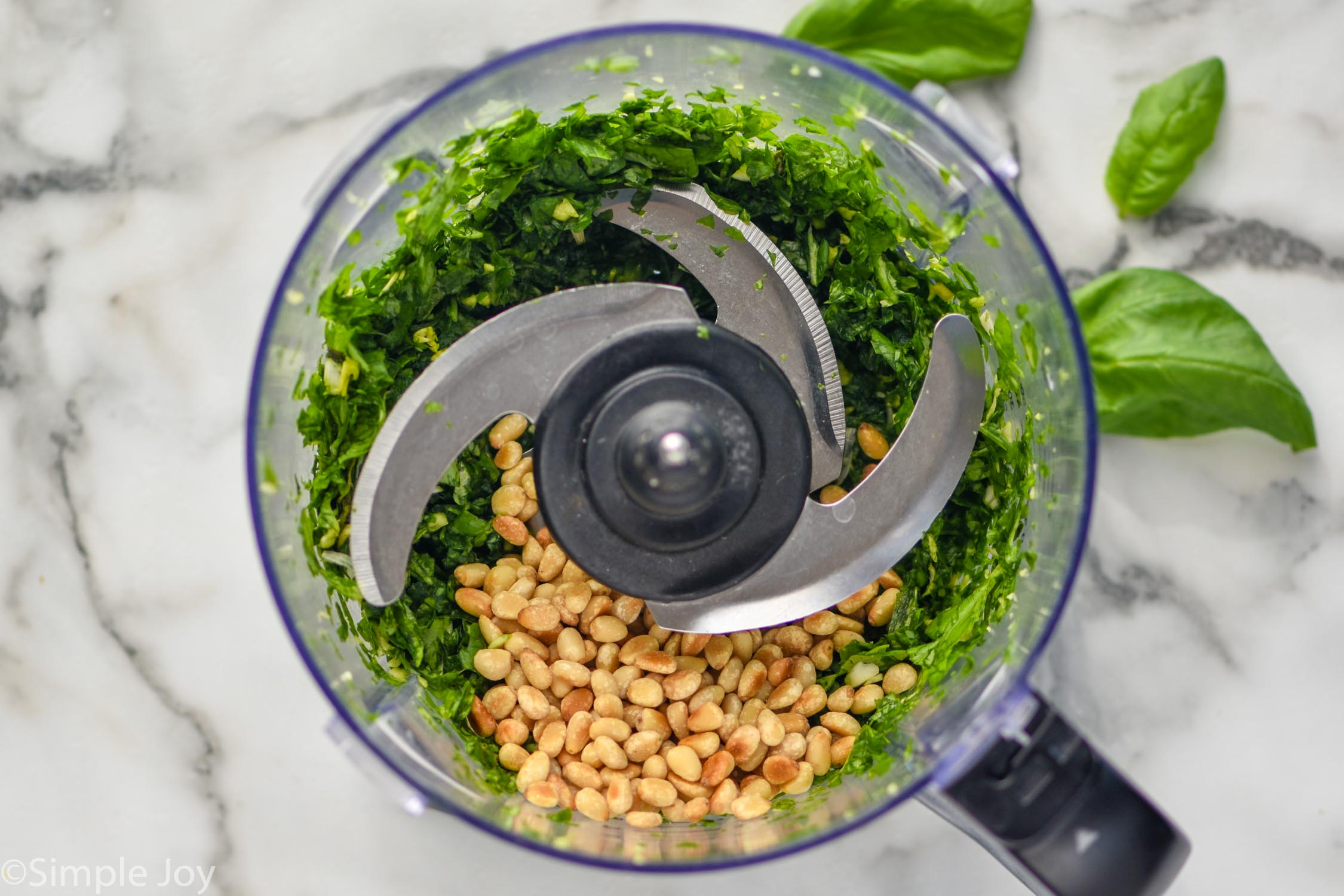Overhead photo of a food processor with ingredients for pesto sauce recipe.