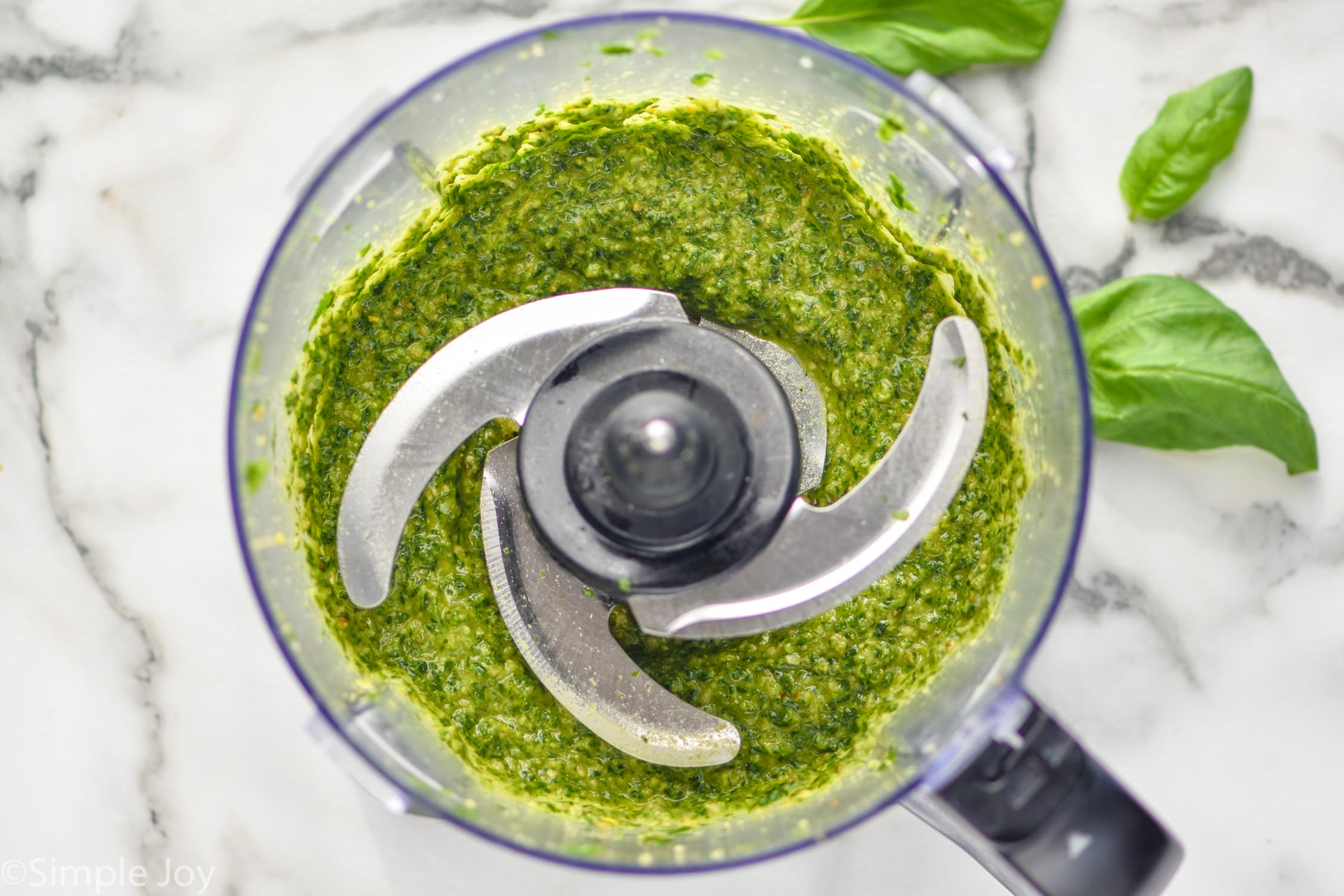 Overhead photo of a food processor with ingredients for pesto sauce recipe.