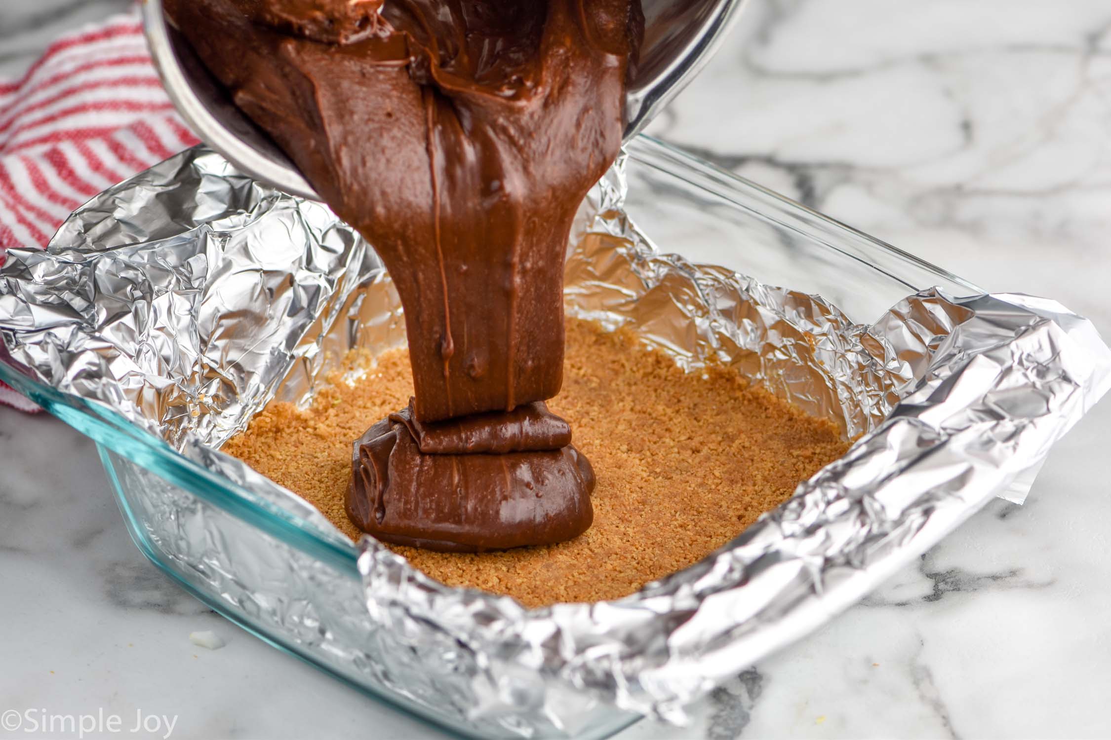 Close up photo of chocolate layer being poured onto graham crust for S'mores Fudge recipe.