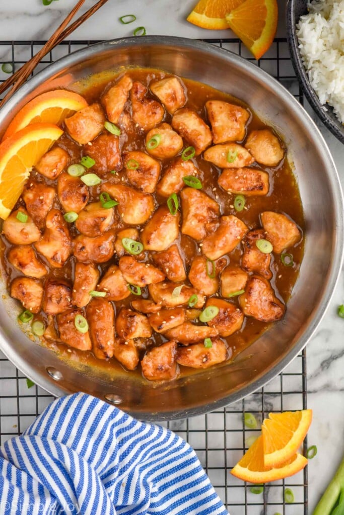Overhead photo of Orange Chicken recipe in a skillet. Bowl of rice beside skillet.
