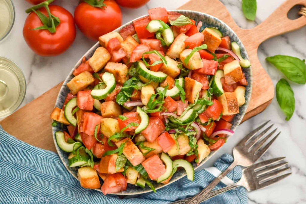 Overhead photo of Panzanella Salad in a bowl. Forks and tomatoes next to bowl.