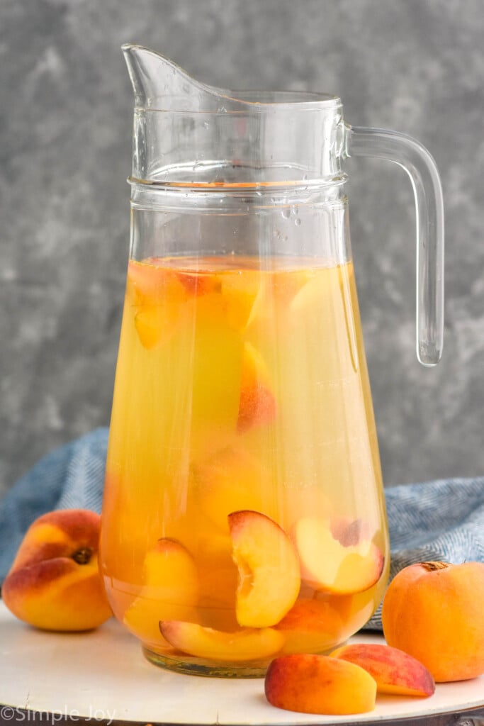 Photo of a pitcher of Peach Sangria Recipe. Peaches beside pitcher.