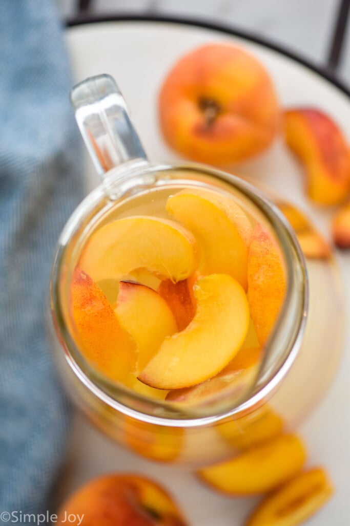 Overhead photo of a pitcher of Peach Sangria Recipe. Extra peaches beside pitcher.