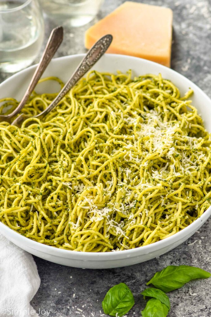 Overhead photo of a bowl of pasta with pesto sauce. Spoons for serving in bowl.