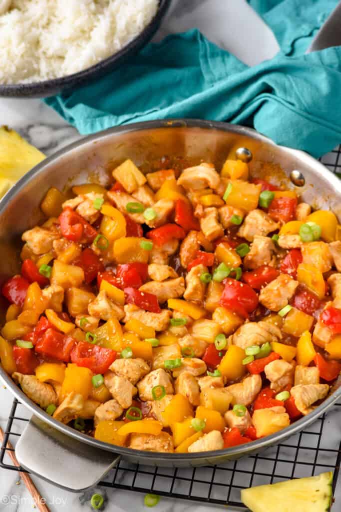 a skillet of pineapple chicken garnished with green onions and sesame seeds