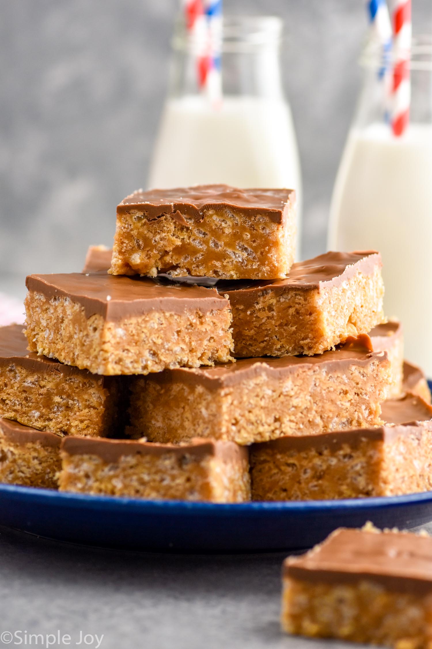 Photo of a plate of Scotcheroos stacked on top of each other. Glasses of milk in the background.