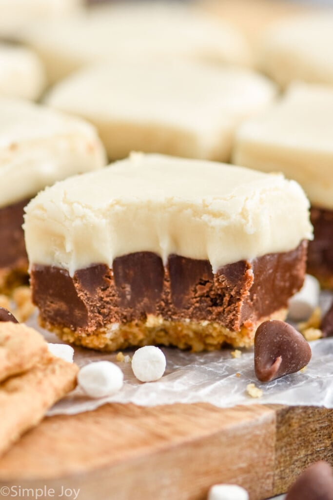 Close up photo of a piece of S'mores Fudge with a bite taken out of it, marshmallows, graham crackers, and chocolate chips.