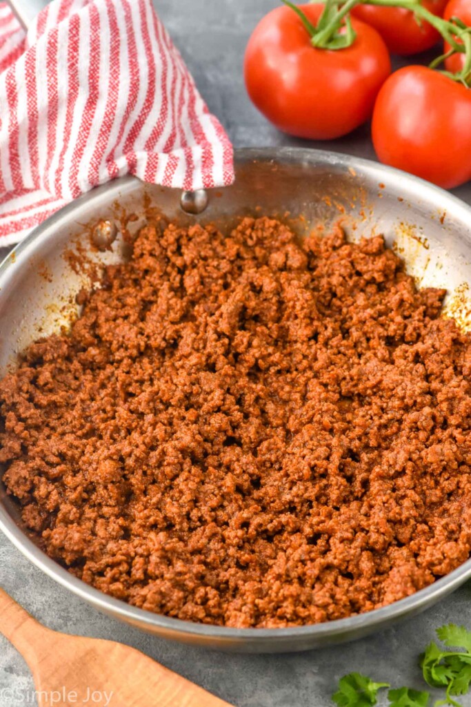 Overhead photo of a skillet of taco meat for Taco Salad recipe. Tomatoes beside skillet.