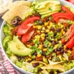 Overhead photo of Taco Salad served in a bowl. Tomatoes, forks, salsa, and sour cream beside bowl.