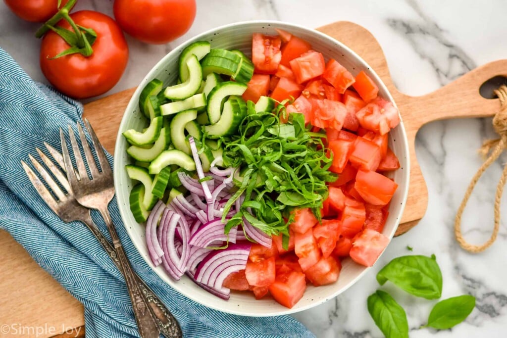 Overhead photo of a bowl of ingredients for Panzanella Salad recipe. Forks and tomatoes next to bowl.