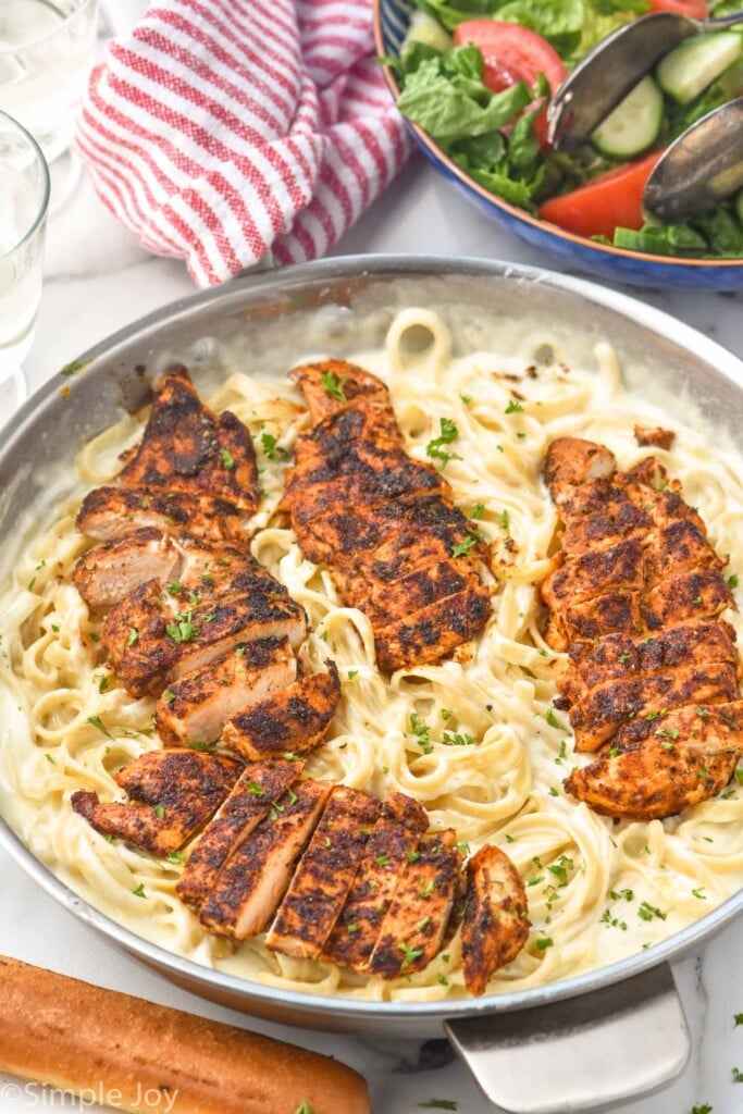 Pan of Blackened Chicken Alfredo with bowl of salad and breadstick sitting beside