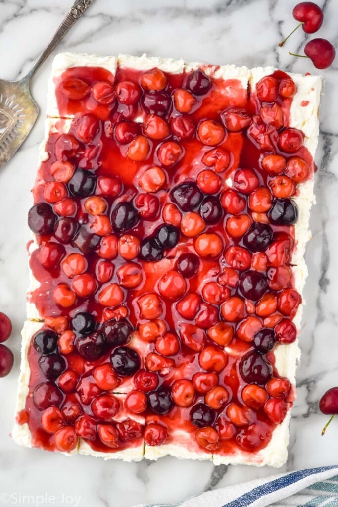 overhead view of cherry cheesecake bars. Serving spatula and fresh cherries sitting beside