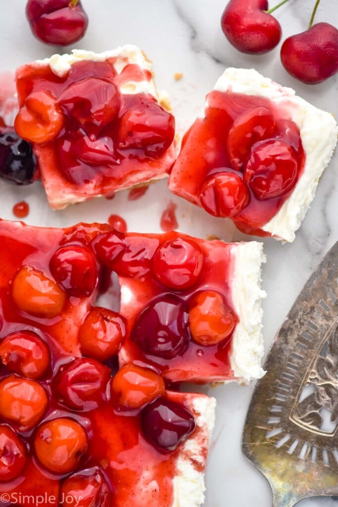 overhead view of cherry cheesecake bars. Fresh cherries and serving spatula sit beside.