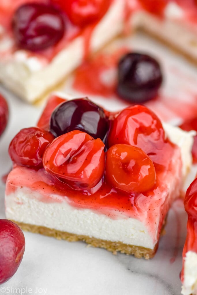 cherry cheesecake bar cut from pan with cherries sitting around in in background