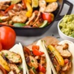 Pinterest graphic for chicken fajitas. Text says "super easy chicken fajitas simplejoy.com" Image shows chicken fajitas in tortillas with bowl of guacamole and grill pan of chicken fajitas sitting in background