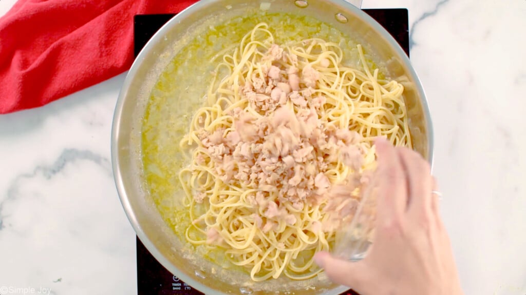 adding clams to a skillet with linguine and sauce