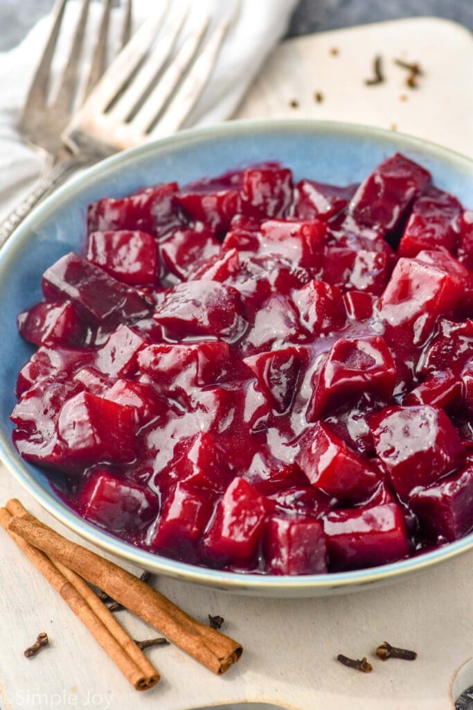 bowl of harvard beets with two forks and two cinnamon sticks sitting beside