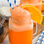 Side view of Orange Creamsicle served in a glass mug garnished with straws and an orange slice. Another glass of Orange Creamsicle on the counter, along with extra orange slices and straws.