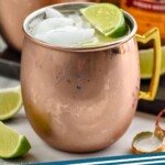 Pinterest graphic for Tequila Mules recipe. Image is side view of copper mugs of Tequila Mule recipe, lime wedges for garnish, and extra bottles of ginger beer. Text says, "Tequila Mules simplejoy.com"