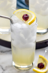 Glass of Tom Collins cocktail with ice, lemon cherry garnish, and straw